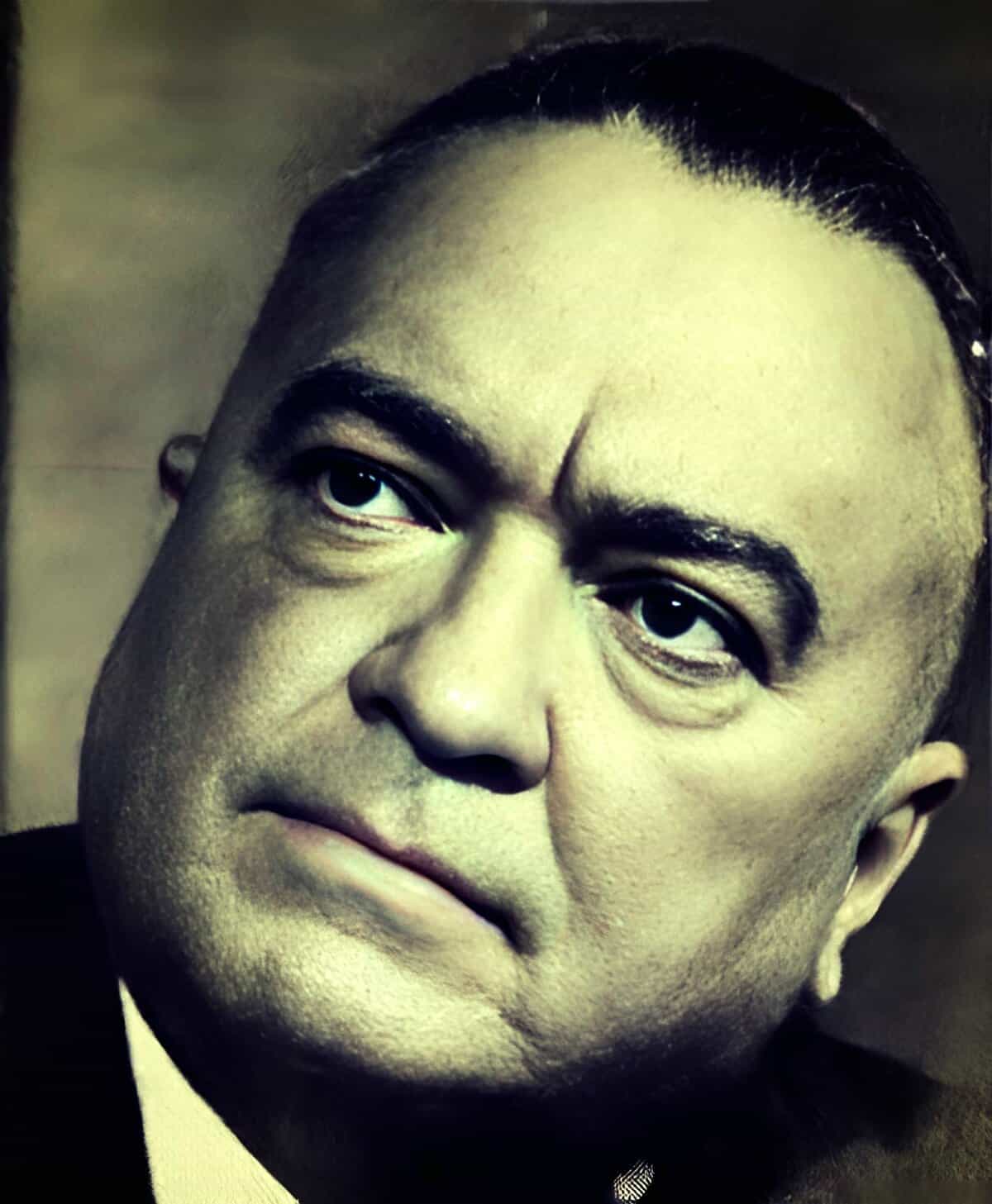 A close-up black and white portrait of a man with slicked-back hair, intense expression, and a prominent scar on his forehead, reflecting historical news and music archive themes.