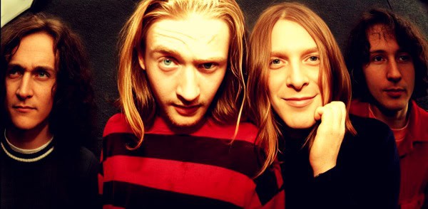 Vintage band portrait featuring four musicians with long hair, representing classic rock or alternative music genre.