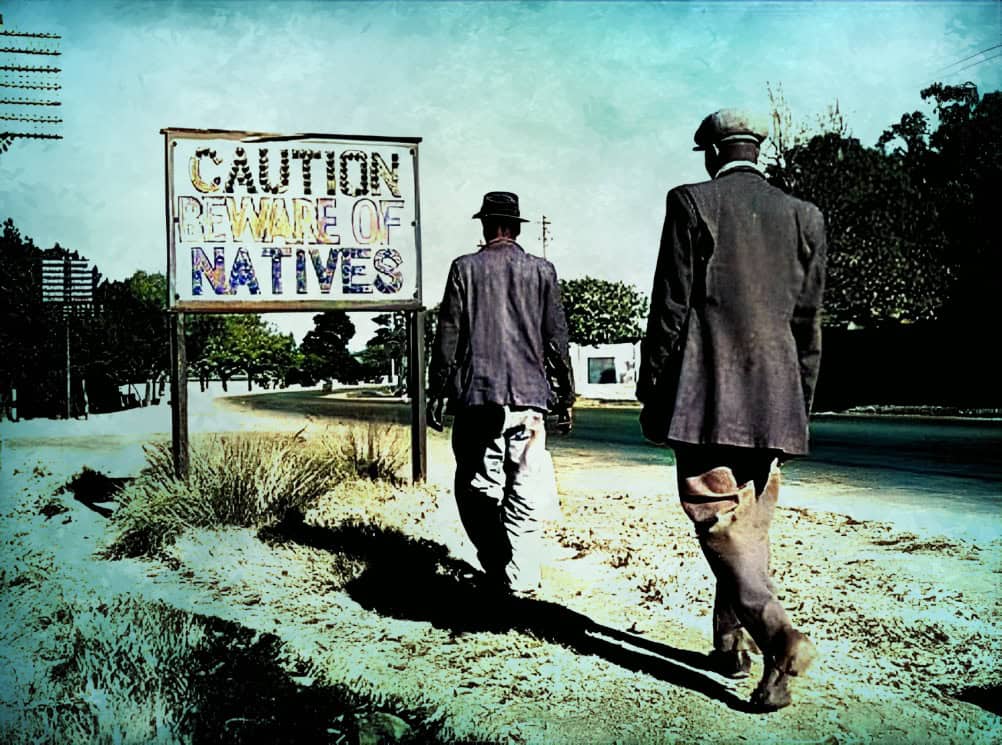 Caution warning sign about natives along a rural road, historical black and white photo, vintage street scene, social commentary on indigenous rights.