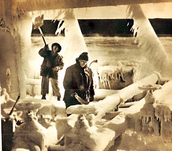 Dark, icy environment with two explorers in heavy winter gear exploring a frozen, snow-covered landscape with large ice formations and crevices.