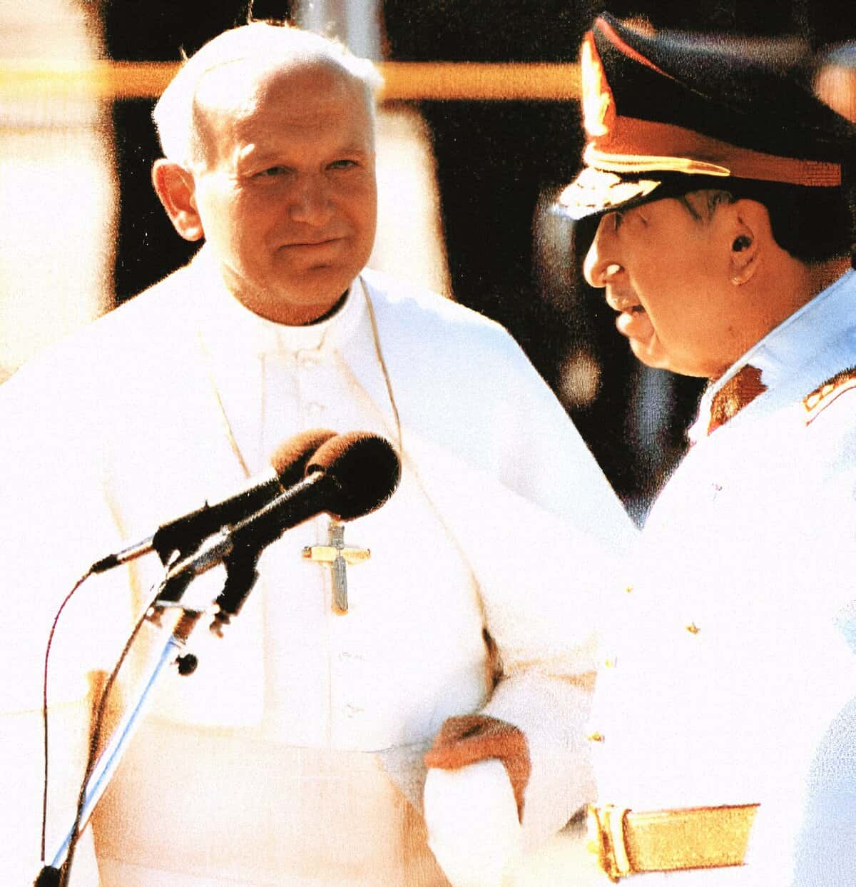 Renowned religious leader Pope John Paul II speaking at a public event, wearing traditional white papal robes and a cross necklace, with a microphone in the foreground, symbolizing history and faith.