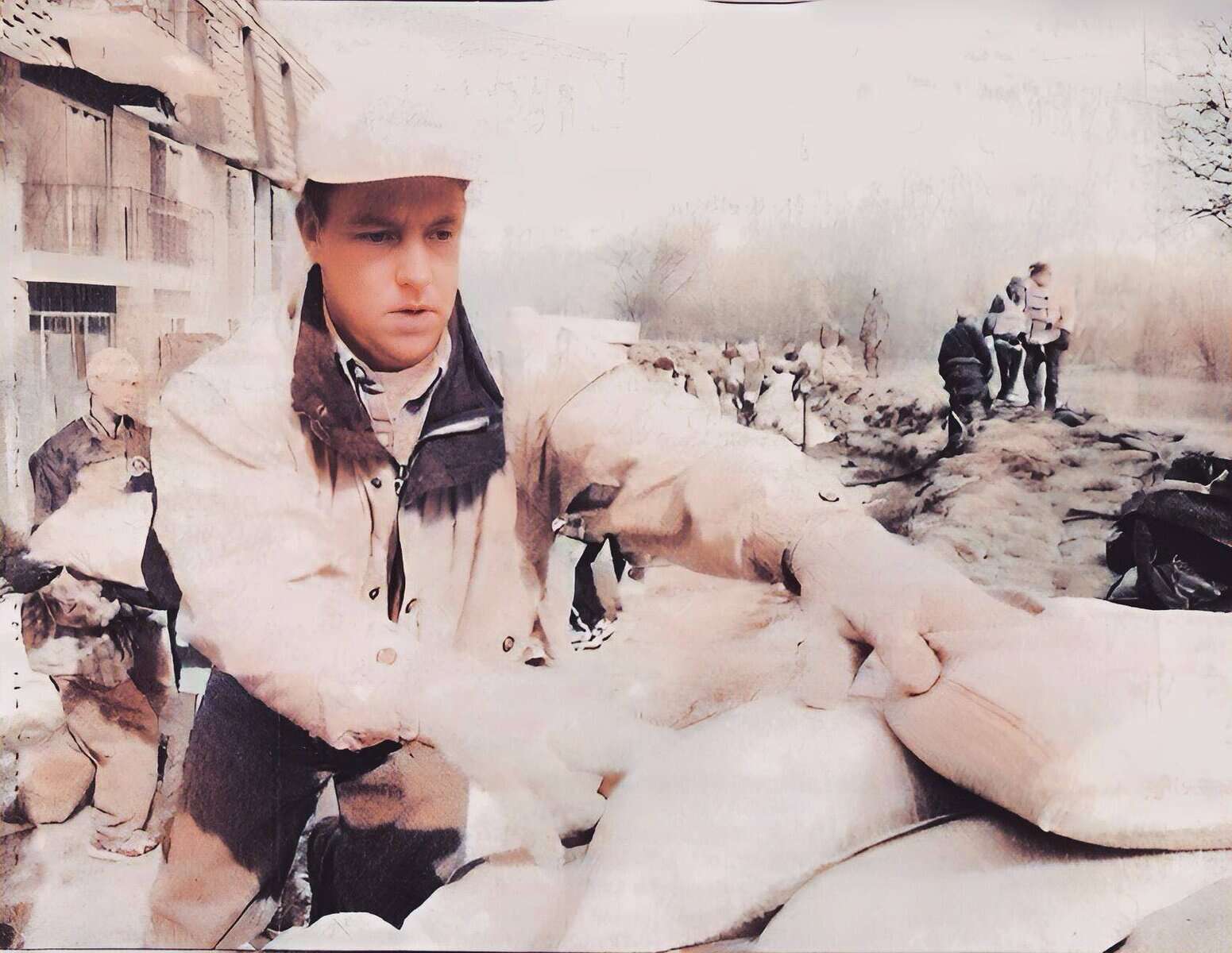 A young man wearing a trench coat and hat working outdoors with sandbags, amidst a scene of historical significance, related to news, history, and music archives.
