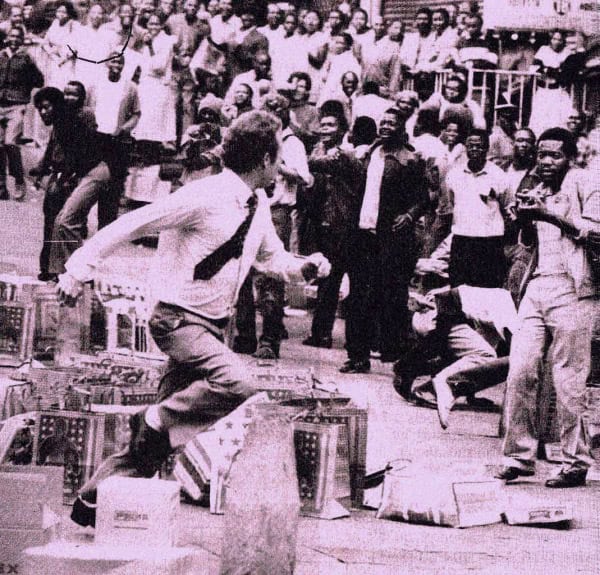 Vivid black and white photo of a lively street protest with a crowd of people and makeshift barricades, capturing historical moments of social movements and community activism.