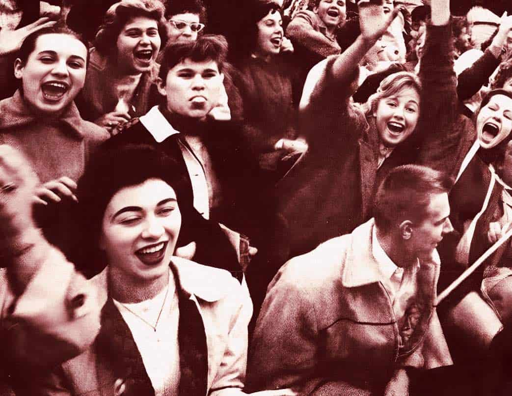 A lively vintage crowd of young people laughing, cheering, and celebrating at a music or historical event, capturing joyful human expression.