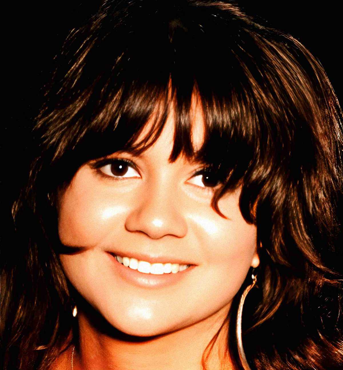 Close-up of a smiling woman with dark brown hair and bright eyes, emphasizing a cheerful expression; suitable for images related to music, news, and history archives.
