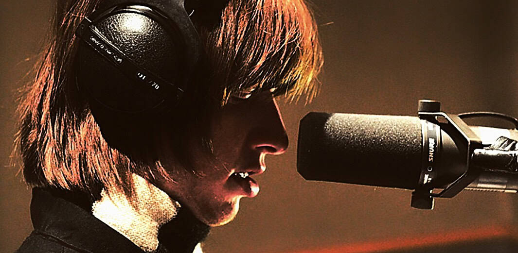 Focused female singer recording music in a professional studio with headphones and microphone, capturing vocals for a music track or broadcast.