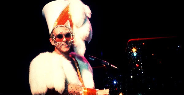 Vintage performer in colorful costume with a tall hat and sunglasses on stage, representing music history and entertainment.