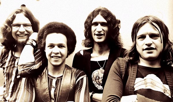 Vintage black and white photo of a rock band with long hair and casual clothing, representing music history and iconic artists.