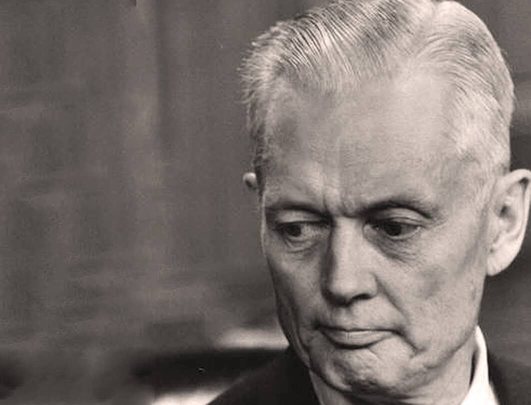A black and white close-up photo of a serious, contemplative elderly man with slicked-back hair, capturing a moment of deep thought or reflection.
