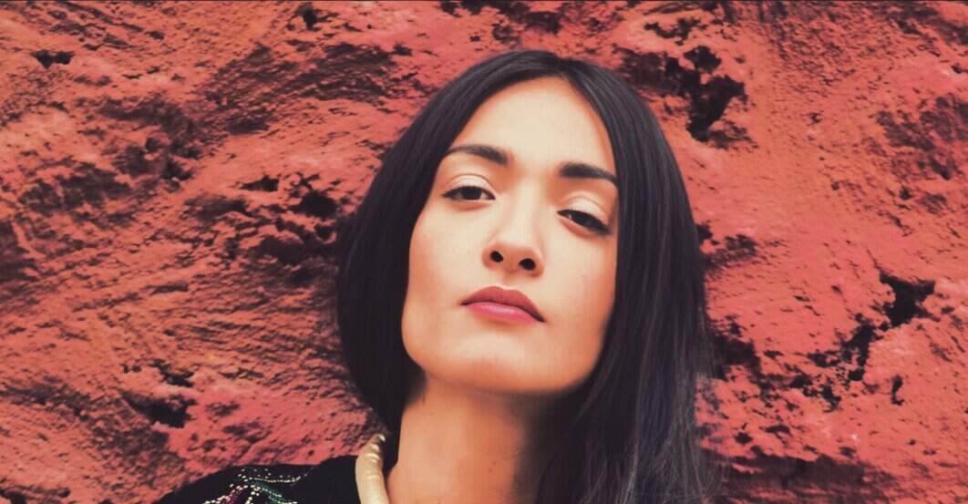 Young woman with long dark hair standing against a textured red rock wall, showcasing a modern, stylish look. Ideal for illustrating contemporary fashion, natural beauty, or outdoor photography.