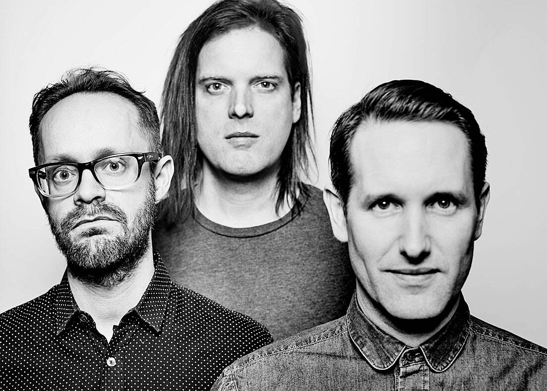 Black and white image of a musical band with three members, showcasing a professional and artistic vibe for music history and sound archive content.
