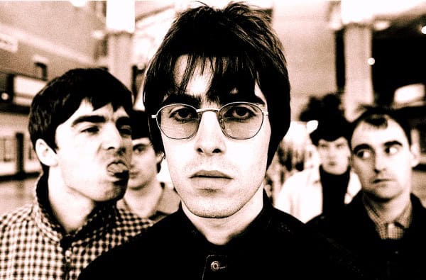 Unrecognized band members with a central figure wearing glasses, set against an urban background, representing music history and archival news coverage.