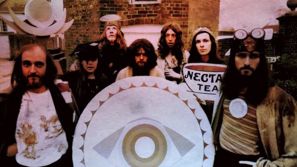 Vintage rock band members posing with a large eye symbol at an outdoor music event, capturing the essence of classic music history and underground music culture.
