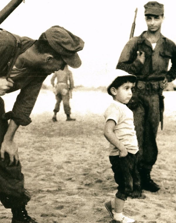 Soldiers interacting with a young boy in a historical military setting, capturing moments related to wartime history and childhood during conflict periods.