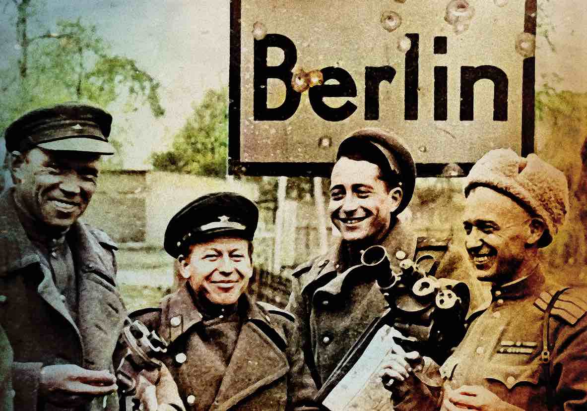 Historic soldiers in WWII uniforms smiling and holding rifles in front of a Berlin sign during World War II.