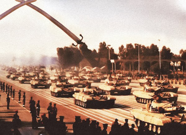 Tanks during a historic military parade, showcasing Cold War era military vehicles and defense history, set against a smoky backdrop with spectators watching from the sidelines.