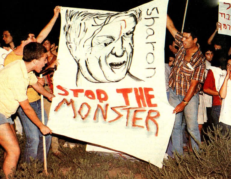 Young protesters holding a large handmade sign with a caricature and the message "Stop the Monster" during a demonstration against nuclear weapons or government policies.