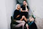 Stylish young women and man sitting on a staircase with grungy walls, representing indie music and youth culture in a contemporary music scene.
