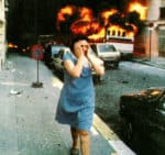 Explosion fire chaos in city street with scared woman covering her ears amidst destruction and debris, iconic image capturing moments of disaster and distress, associated with historical news reports and emergency response.