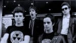 A black and white photo of a punk rock band with four members wearing leather jackets and sunglasses, showcasing music history and classic rock culture, perfect for archives of 1980s music and news.