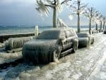 Frozen cars covered in ice and snow along a seaside promenade during a severe winter storm.
