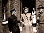 Police officer woman woman and man in conversation outside brick building historical black and white photo.