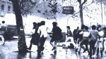 Children playing and dancing in the rain near a Metro station in black and white, capturing a nostalgic moment of urban life and community during rainy weather.