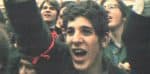 Young woman protesting at a rally, expressing emotions of passion and activism, surrounded by diverse crowd, capturing the spirit of social movements, news, and history coverage.