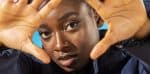 Vibrant portrait of an African American woman making a heart shape with her hands, emphasizing diversity, self-love, and empowerment; perfect for music, news, and history archive content.