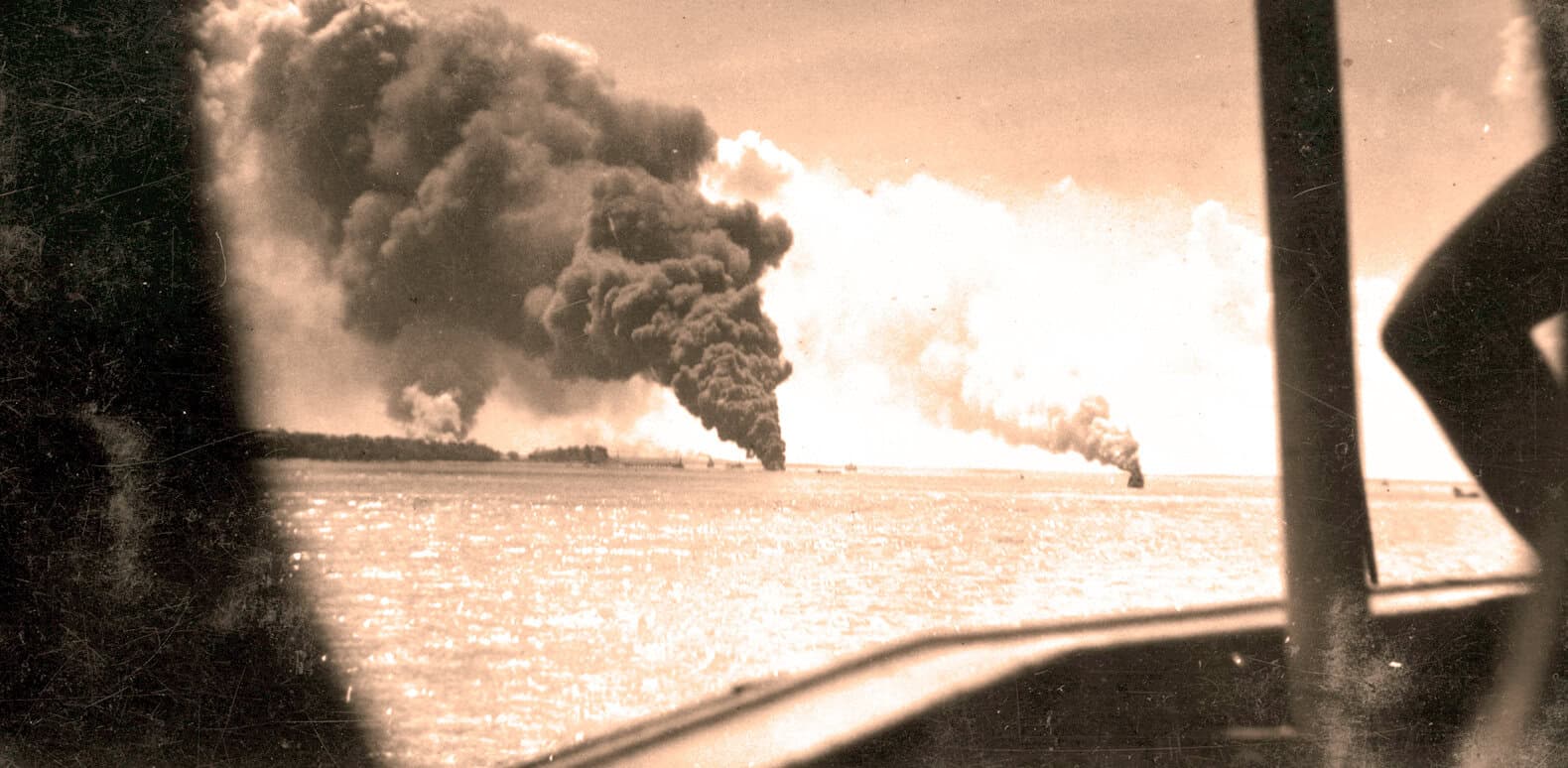Explosive fire and thick smoke rising over water, historic incident captured from a boat during a significant news event.
