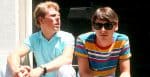 Young men in casual summer clothing, one wearing sunglasses, sitting in front of a black door, representing 80s pop culture and music history, with a nostalgic vibe.