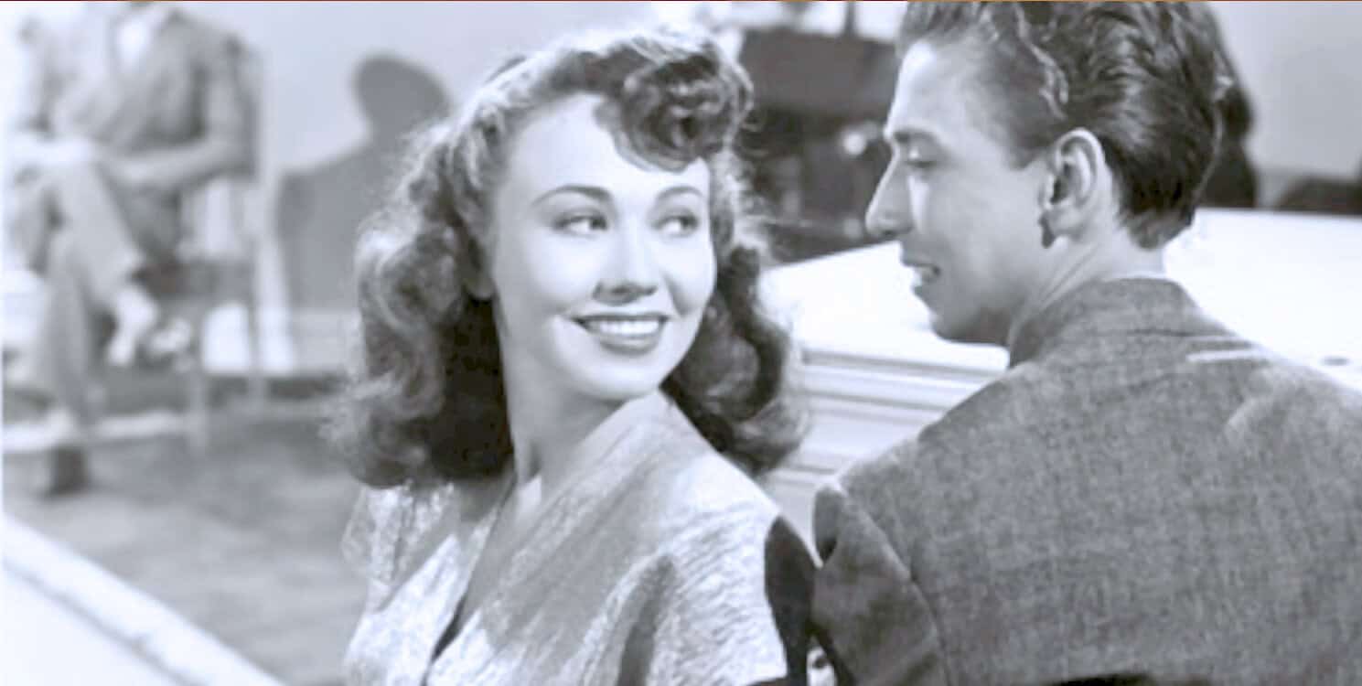 Vintage black and white image of a romantic scene from the 1950s, featuring a smiling woman and a man sharing an intimate moment, representing classic movie stars, nostalgia, and mid-20th-century entertainment.
