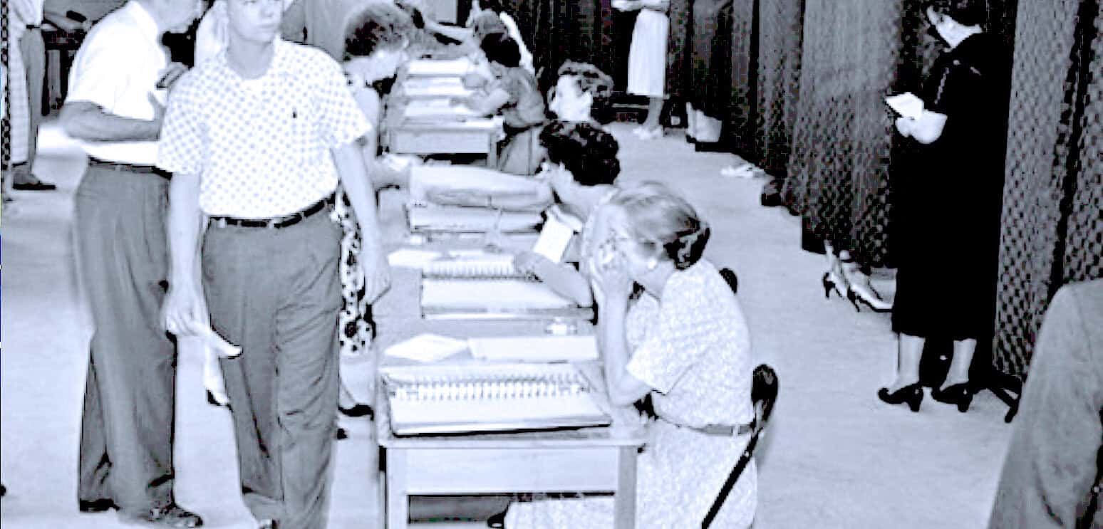 Old black and white photo of people voting at a polling station in the 1960s, highlighting historical elections, civic engagement, and voting process.