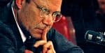 Thoughtful man in glasses with finger to lips, symbolizing silence or reflection, speaking at a news or history event, captured for a sound archive of news, history, and music.