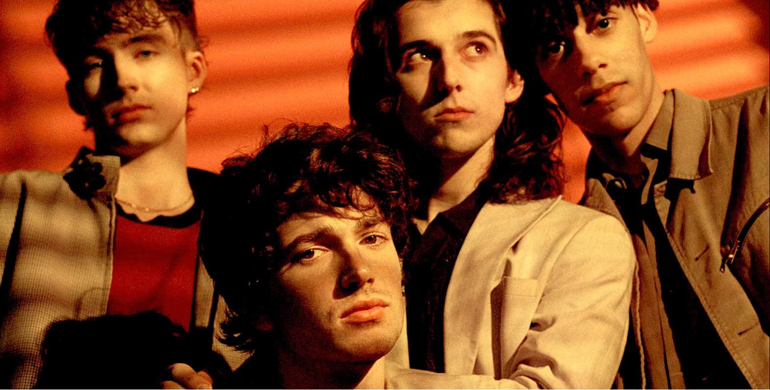 A rock band with four members, showing a vintage 1990s style, posed against a warm, red-toned background, illustrating music history and classic band photography.
