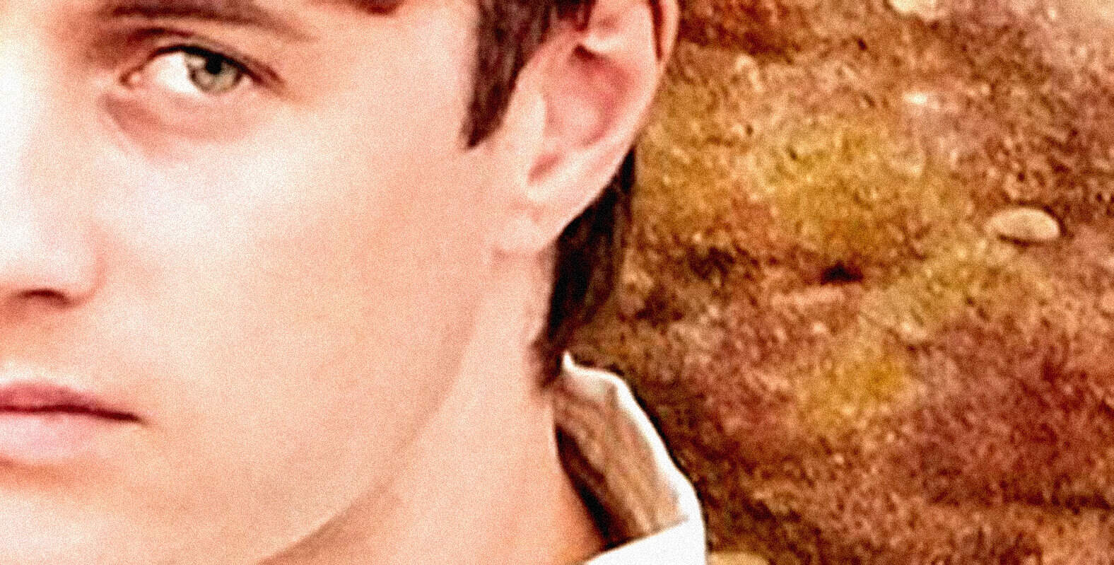 Close-up of a person's face, highlighting an eye and facial features, with a textured earthy background, representing themes of news, history, and music from the Past Daily sound archive.