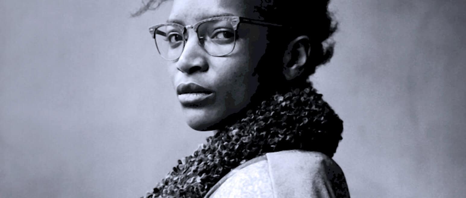 Elegant woman wearing glasses and a scarf, black and white portrait, reflective expression, representing classic news, history, and music archive content.