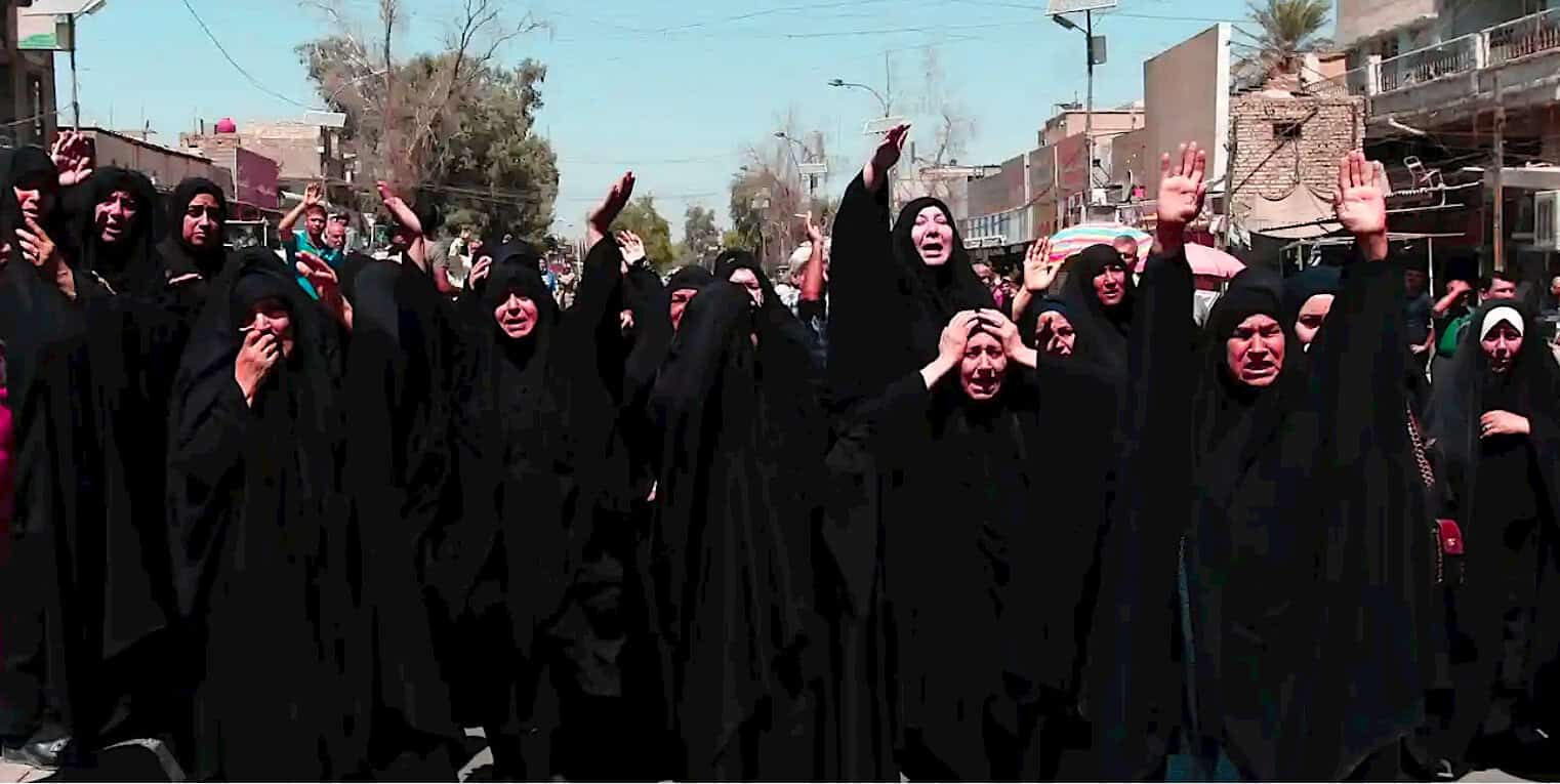 Women wearing black chadors protesting in the street with emotional expressions and raised hands, demonstrating a social or political demonstration.