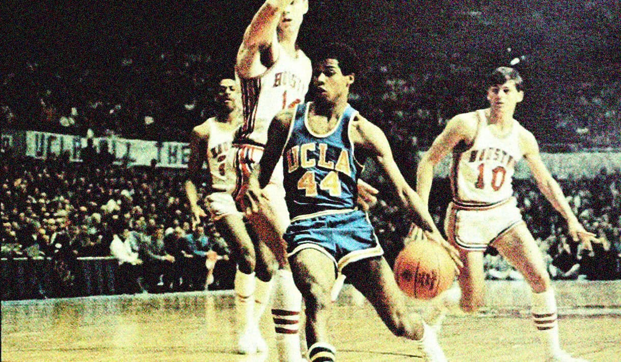 UCLA Bruins basketball player driving to the basket during a game, with defenders attempting to block shot, highlighting historic sports moments and classic basketball action.
