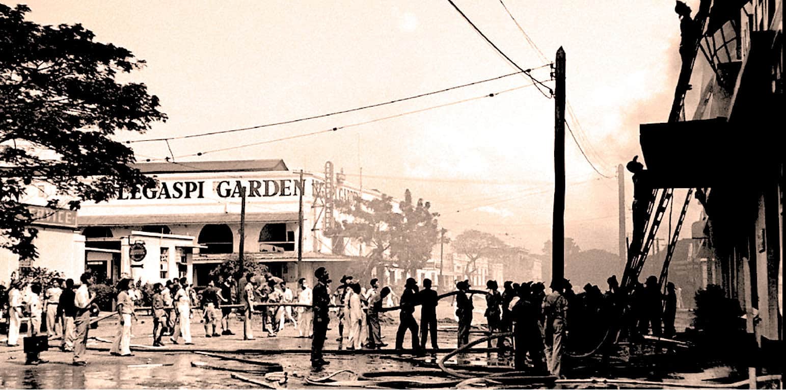 Firefighters battling a blaze on a city street with smoke and emergency responders, historic photograph capturing news and history moments, reminiscent of past daily sound archive of news and music.