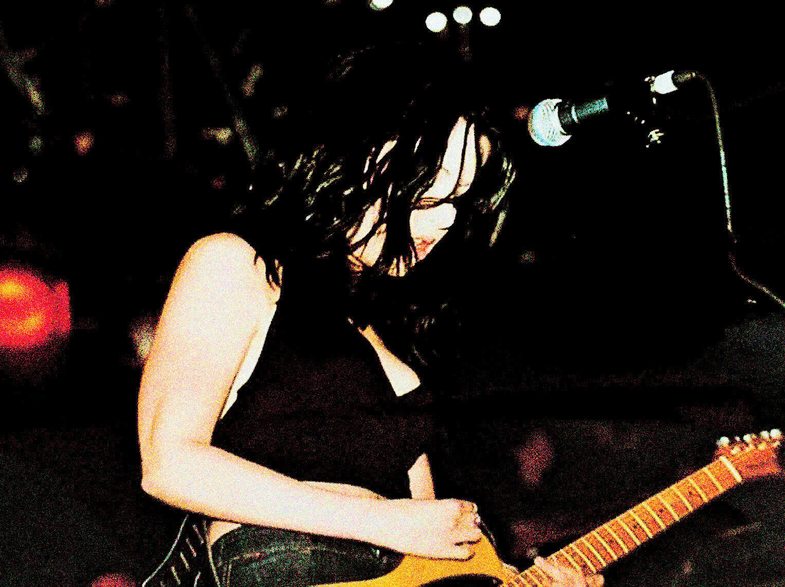 Guitarist woman performing live on stage with microphone, dark background, music event, acoustic guitar, female musician, concert, music performance, venue lighting, live music scene.