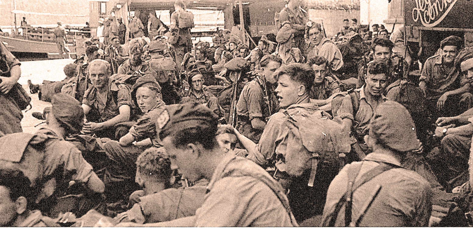 Boy scouts gathering at a World War II event, wearing uniforms, backpacks, and hats, with a crowd of fellow scouts in the background during a historic wartime rally.