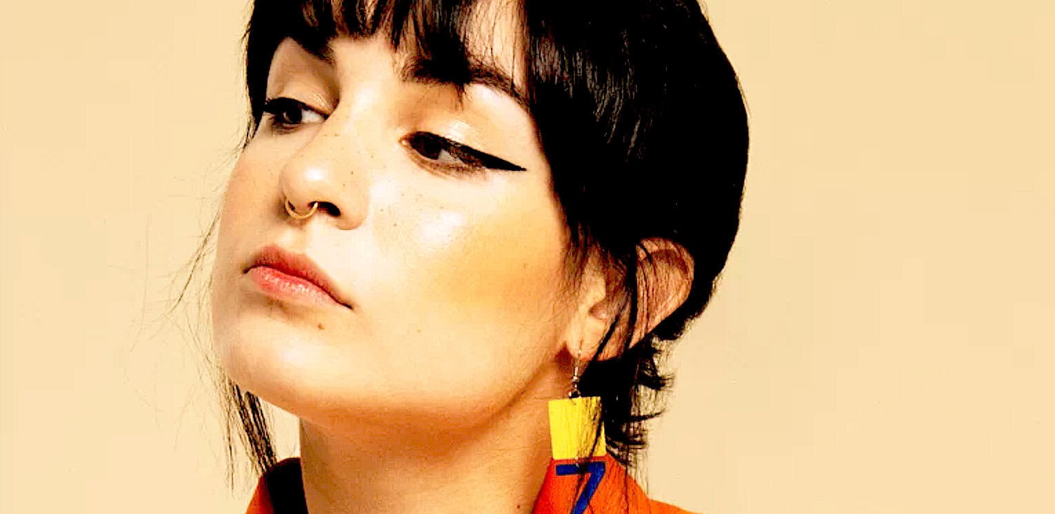 Bold, modern portrait of a woman with short dark hair and geometric earrings, highlighting artistic fashion, makeup, and contemporary style. Perfect for music and news archives.