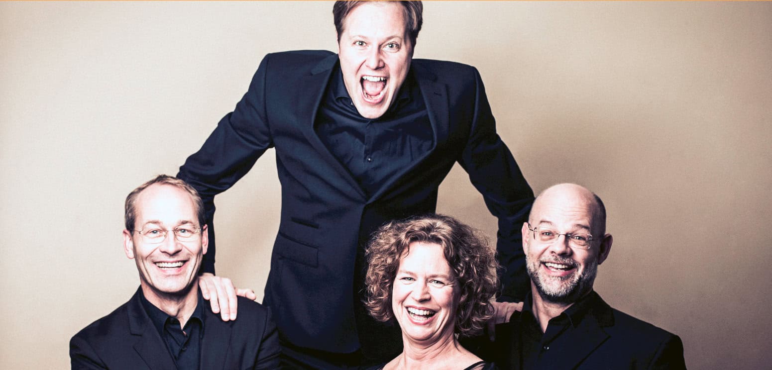 Man in business suit shouting in studio with three smiling people, representing news, history, and music archives.
