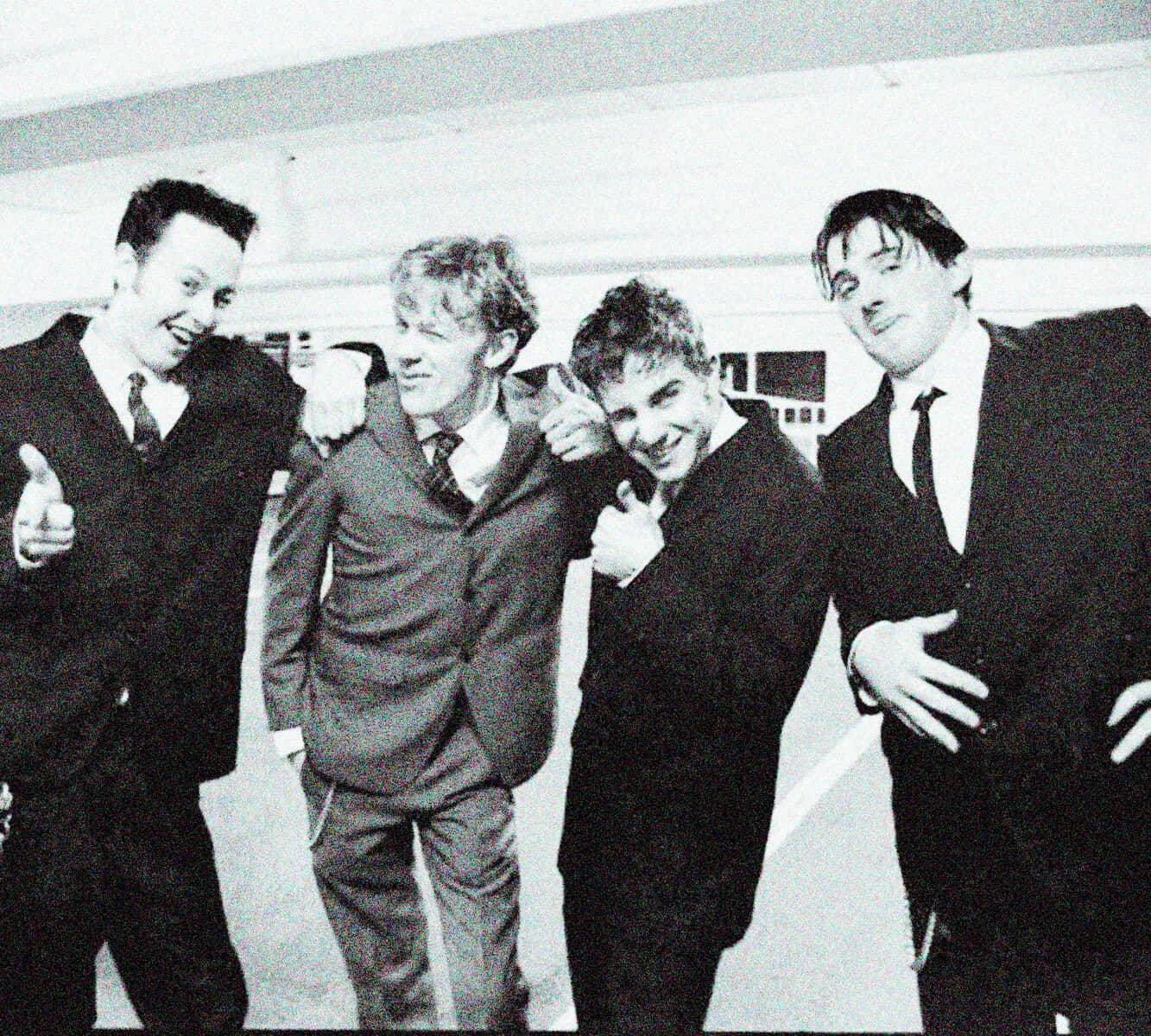 Black and white photo of 4 young men in suits smiling and posing together, nostalgic image of music and pop culture, vintage style, cool vibe, retro fashion.