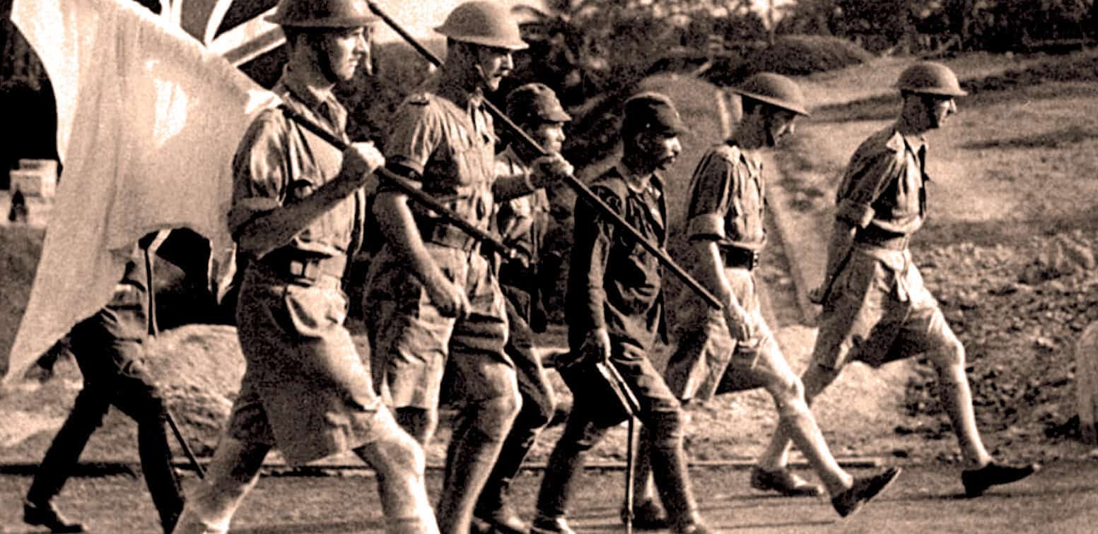 Soldiers marching during wartime, black and white historic military photo, World War II era, soldiers wearing helmets, carrying a flag, military history, news archive, music, and historical recordings.