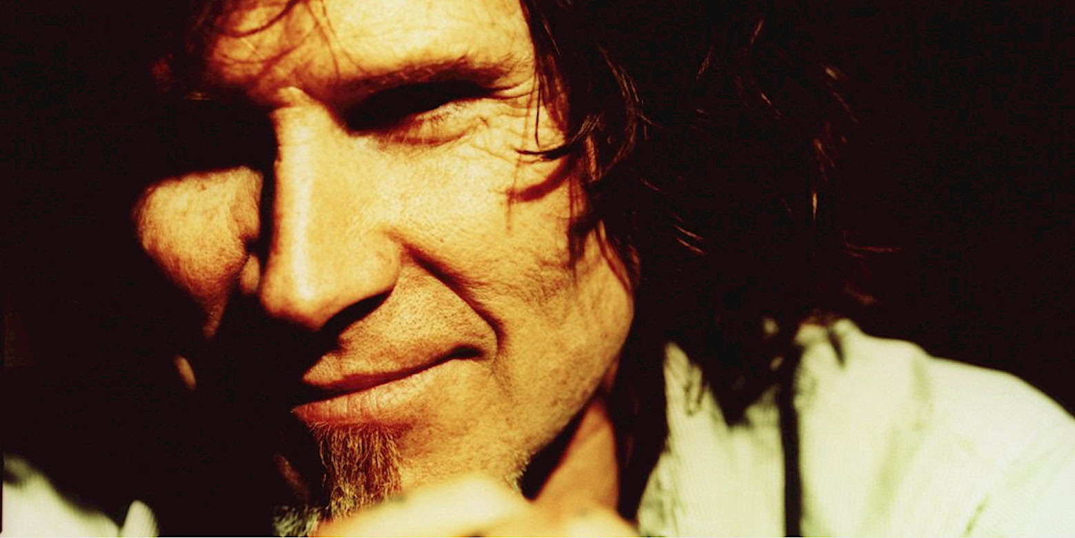 Close-up of a smiling man with long dark hair, emphasizing musical and nostalgic themes related to historical news, music, and sound archives.