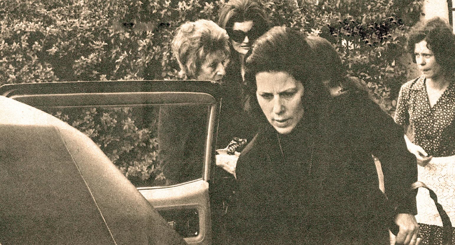 Vintage photograph of women with dark hair and sunglasses gathered around a car, capturing a moment from mid-20th-century social scene.