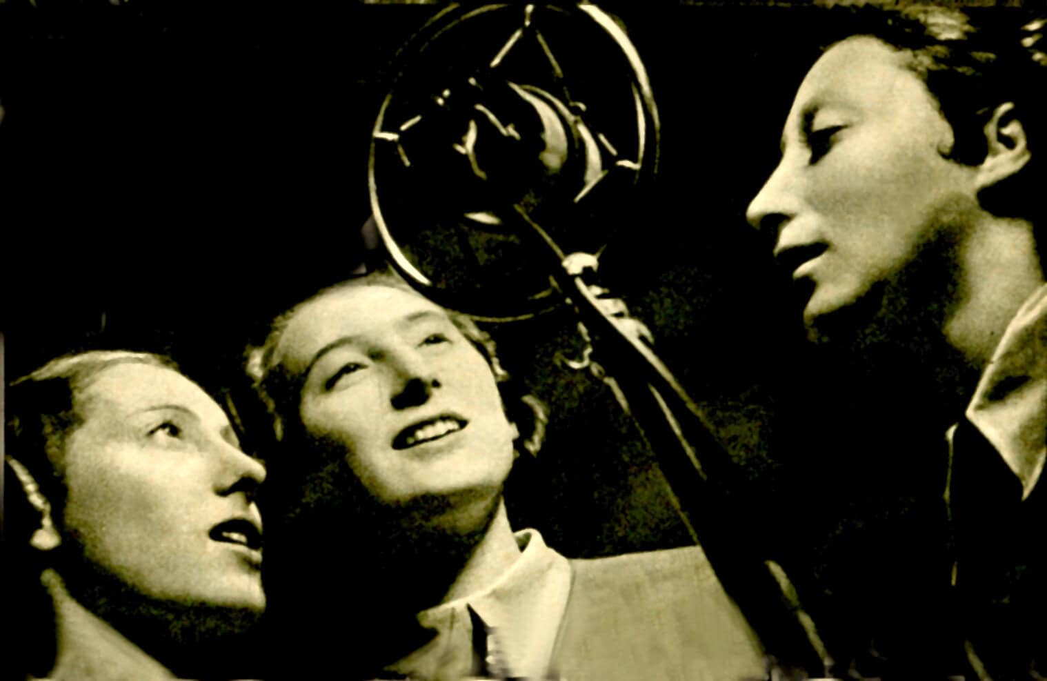 Close-up of three vintage women and a man with a microphone, singing or speaking into a vintage microphone, representing classic news, history, and music archives from Past Daily.