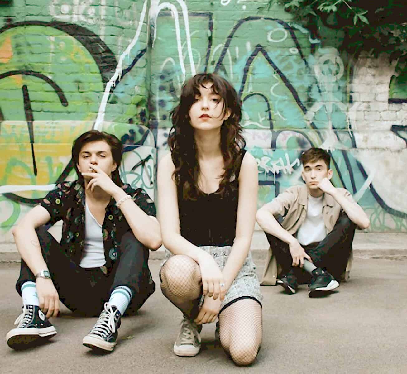 A vibrant band of three young musicians posing in front of a colorful graffiti mural, highlighting their indie style and urban setting perfect for music and history archive content.